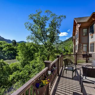 A scenic view from a wooden deck overlooking lush greenery and distant mountains under a clear blue sky.