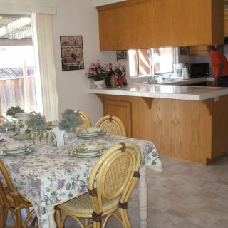 A cozy dining area with a floral tablecloth set for a meal, adjacent to a kitchen with wooden cabinets.