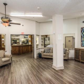 A spacious lobby with comfortable seating and a wooden floor, featuring a reception desk and ceiling fan.