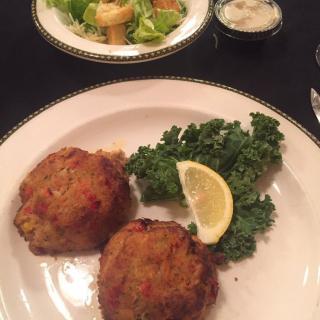 A plate of crab cakes garnished with parsley and a lemon wedge, accompanied by a side salad.