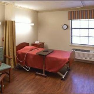 A clean and organized hospital room with a bed and wooden flooring.