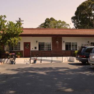 A small one-story building with a parking lot and cars in front, surrounded by trees.