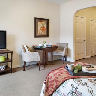 A cozy bedroom with a small seating area, featuring a TV, chairs, and decorative elements.