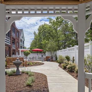 A scenic outdoor garden with a winding pathway, surrounded by trees and bordered by buildings.