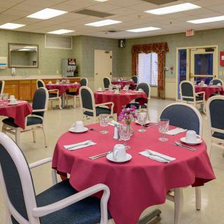 A neatly arranged dining area with tables covered in red tablecloths, set with cups and saucers.