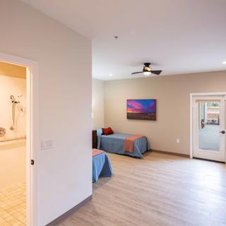 A spacious and modern bedroom featuring a blue bedspread, artwork on the wall, and natural light.