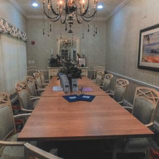 A well-decorated dining room featuring a long table with multiple chairs, ornate chandelier, and framed artwork on the wall.