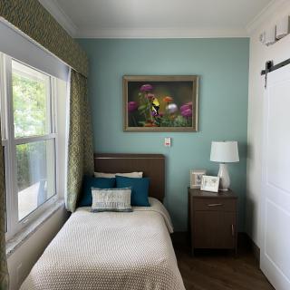 A cozy bedroom with a single bed, nightstand, and a lamp by the window.
