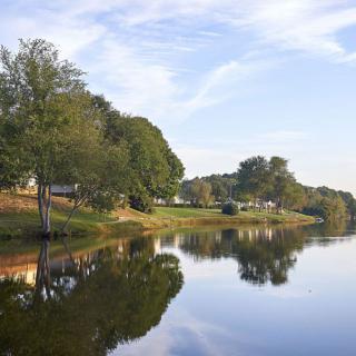 A serene lakeside view with houses and trees reflected in the calm water.