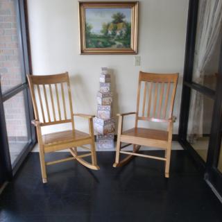 Two wooden rocking chairs placed in a cozy corner with a framed painting on the wall.