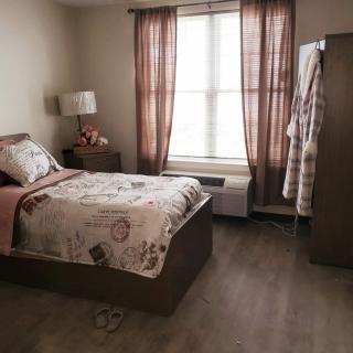 A cozy bedroom with a single bed, nightstand, and wardrobe near a window with curtains.