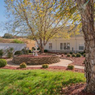 A beautifully landscaped garden with a central fountain, surrounded by trees and shrubs, leading to a residential building.