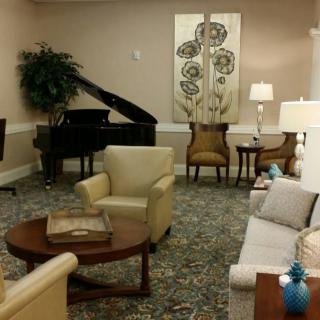 A cozy living room with a grand piano and comfortable seating, elegantly decorated with lamps and artwork.