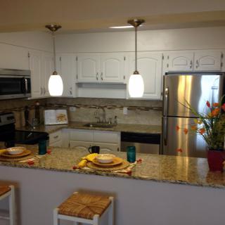 A modern kitchen with white cabinets, stainless steel appliances, and pendant lighting over a decorated countertop.