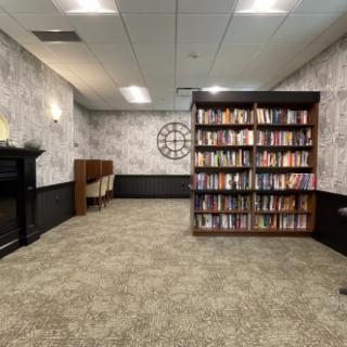A cozy library room with a large bookshelf, comfortable seating, and a decorative wall clock.