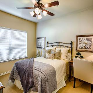 A cozy bedroom featuring a neatly made bed with pillows and a blanket, complemented by framed artwork on the walls and a ceiling fan overhead.
