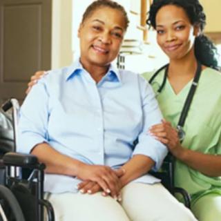 A healthcare professional smiling with a patient in a wheelchair.