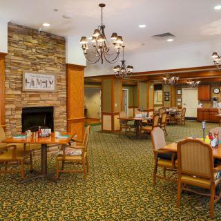 A cozy dining area featuring elegant chandeliers, a stone fireplace, and neatly arranged tables and chairs.
