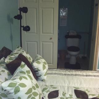 A bedroom with a floral-patterned bedspread, adjacent to a bathroom with a visible toilet.
