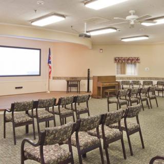 An empty conference room with rows of chairs facing a projector screen and an American flag.