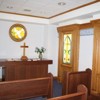 A small chapel featuring an altar with a cross and stained glass windows.