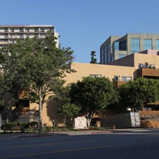 An urban street view featuring multiple buildings and trees under a clear blue sky.