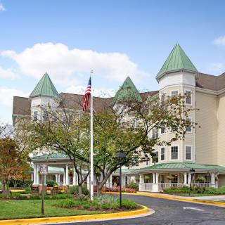A large, elegant building with green conical roofs, surrounded by trees and featuring an American flag in front.