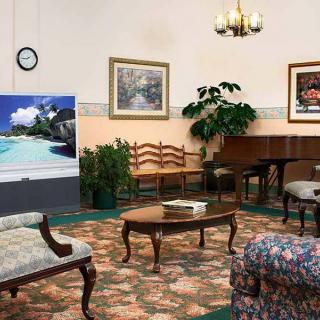 A classic-style living room featuring a sofa, coffee table, piano, and various paintings on the walls.