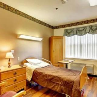 A well-lit hospital room with a single bed, wooden furniture, and a window with curtains.