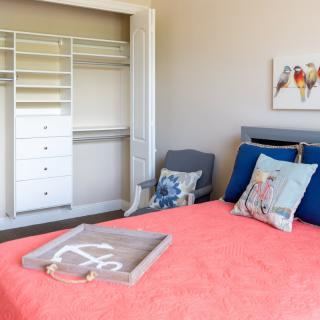 A cozy bedroom with a coral bedspread, decorative pillows, and an open closet.