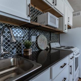A modern kitchen with a black countertop, stainless steel sink, and geometric backsplash.