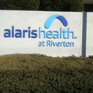 A sign for Alaris Health at Riverton surrounded by bushes.