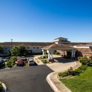 A large building with a main entrance and surrounding driveway on a sunny day.