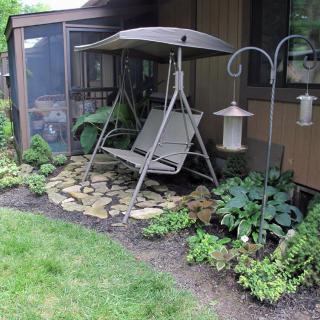 A cozy garden area featuring a swing seat with a canopy, surrounded by plants and landscaping, complete with a bird feeder.