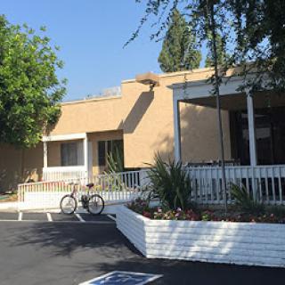 A sunny view of a building with a bicycle parked outside, surrounded by greenery.