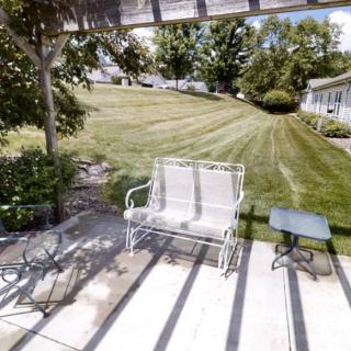 A peaceful backyard patio with a bench, table, and a well-manicured lawn.
