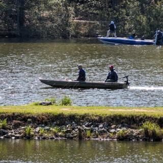 Two people enjoy a day on the water in a small boat while another boat is visible in the background.