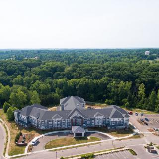 Aerial view of a large building surrounded by lush greenery and a parking lot.