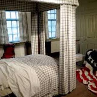 A cozy bedroom featuring a four-poster bed with plaid curtains and a patriotic-themed blanket.