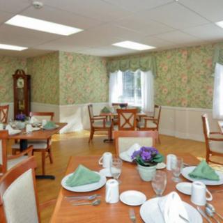 A well-lit dining room with neatly arranged tables and chairs, featuring elegant table settings and decorative wallpaper.