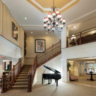 A luxurious lobby featuring a grand staircase and a black piano beneath a stunning chandelier.