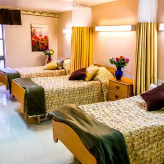 A brightly lit hospital room with multiple beds, flowers, and neatly arranged furnishings.