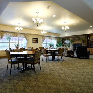 A spacious dining area with multiple tables and chairs, illuminated by chandeliers and natural light from large windows.