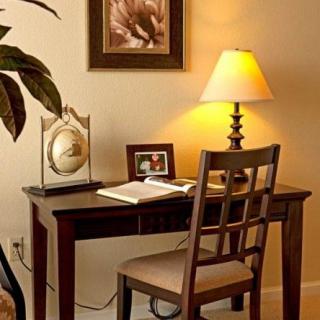 A cozy home office setup with a wooden desk, chair, and a lamp providing warm lighting.