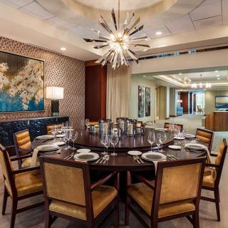A luxurious dining room with a round table elegantly set for a meal, featuring a modern chandelier and sophisticated decor.