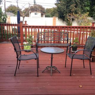 A wooden patio deck with two chairs and a round table, decorated with potted plants.