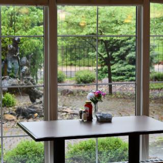 A serene view from inside, showcasing a table adorned with flowers and an inviting garden landscape beyond the window.