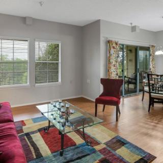 A modern living room with a colorful rug, red chair, and a glass coffee table, adjacent to a dining area with large windows.