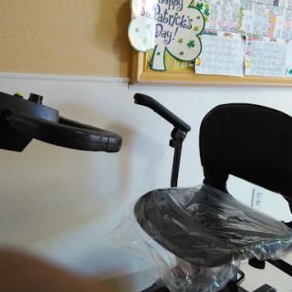 An office wheelchair partially wrapped in plastic, set against a wall with a calendar.