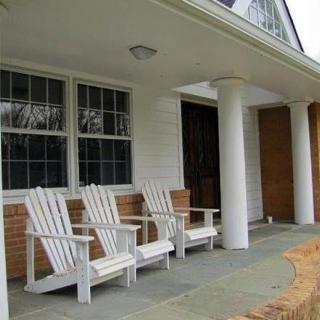 A porch with white Adirondack chairs and columns.